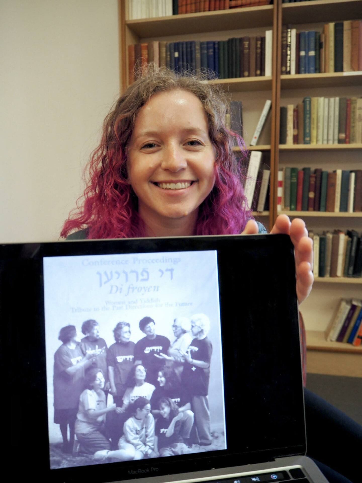 <p>Sarah Biskowitz poses with a digitized copy of *Di Froyen*. Photo credit: Cameron Bernstein.</p>