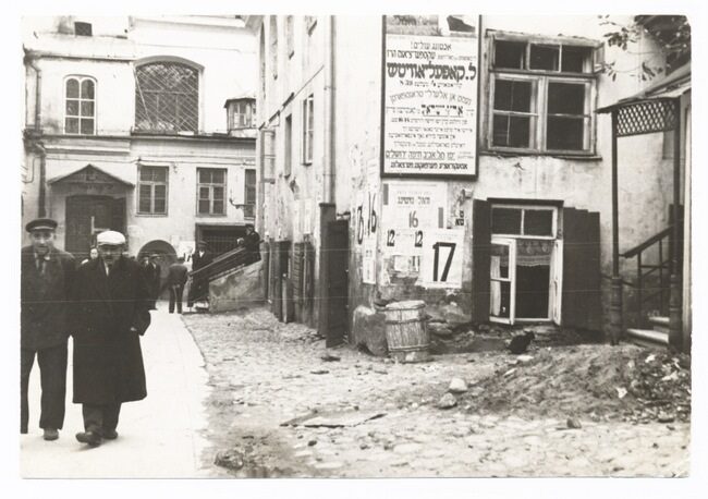 <p>The <em>shulhoyf, </em>synagogue courtyard, Vilna, 1930s, showing a Yiddish advertisement for shipping agent L. Kopelovitsh. Source: YIVO Archives.</p>