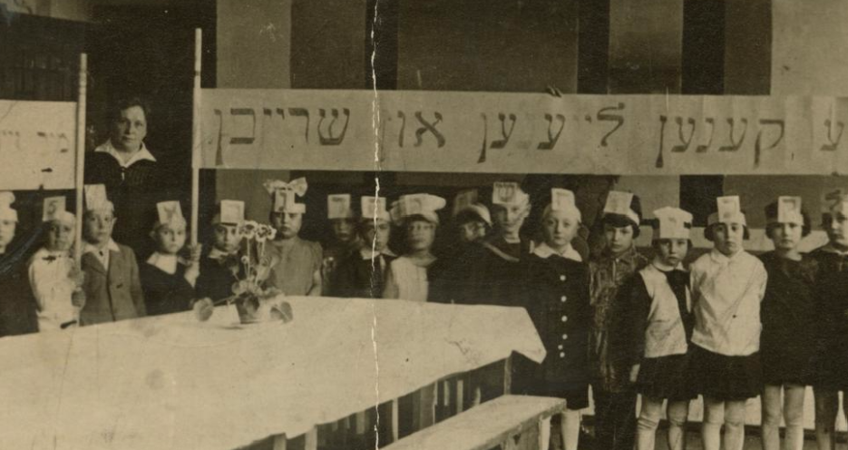 <p>Stefania Shifra Szabad with a class in a Yiddish school, Wilno, 1929. Children hold a banner that reads: “We can all read and write.” (Courtesy of YIVO)</p>